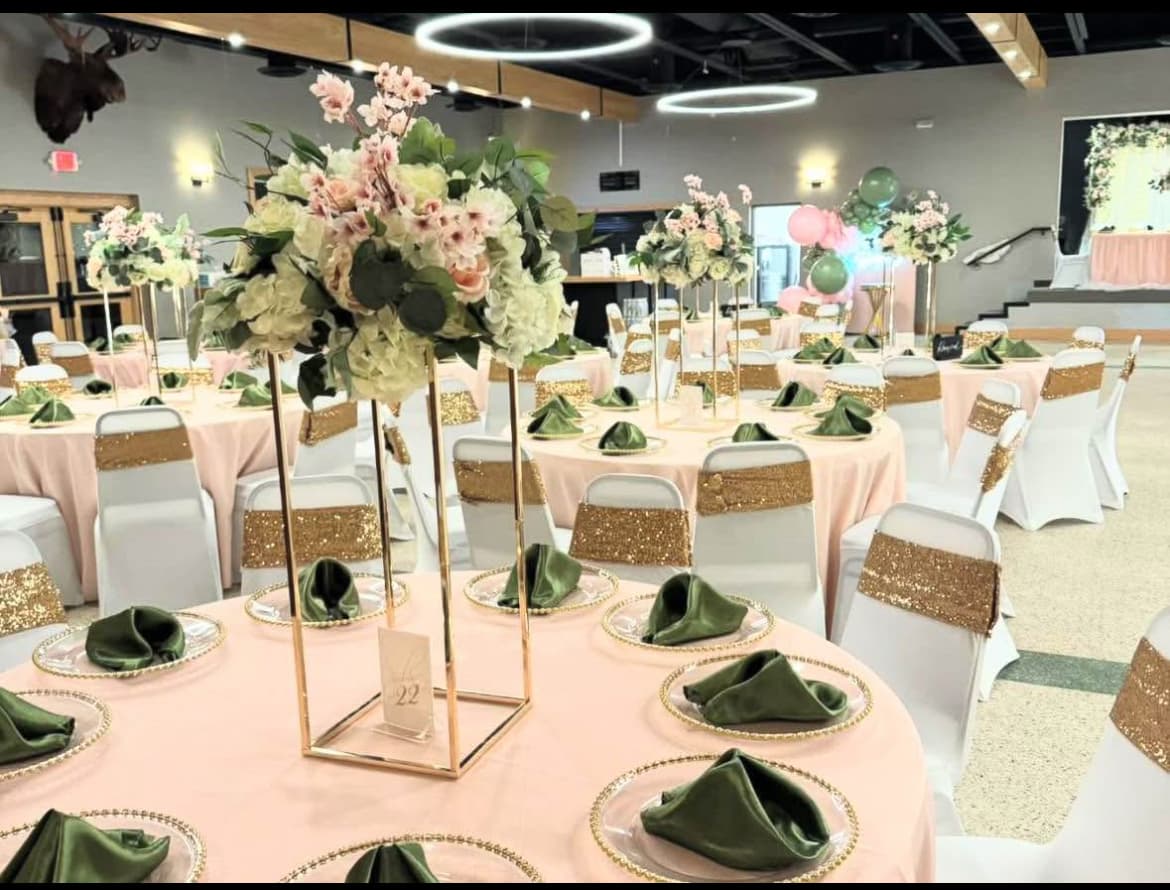 Pink banquet tables with green napkins, tall gold floral centerpieces, and gold-sequined white chairs.