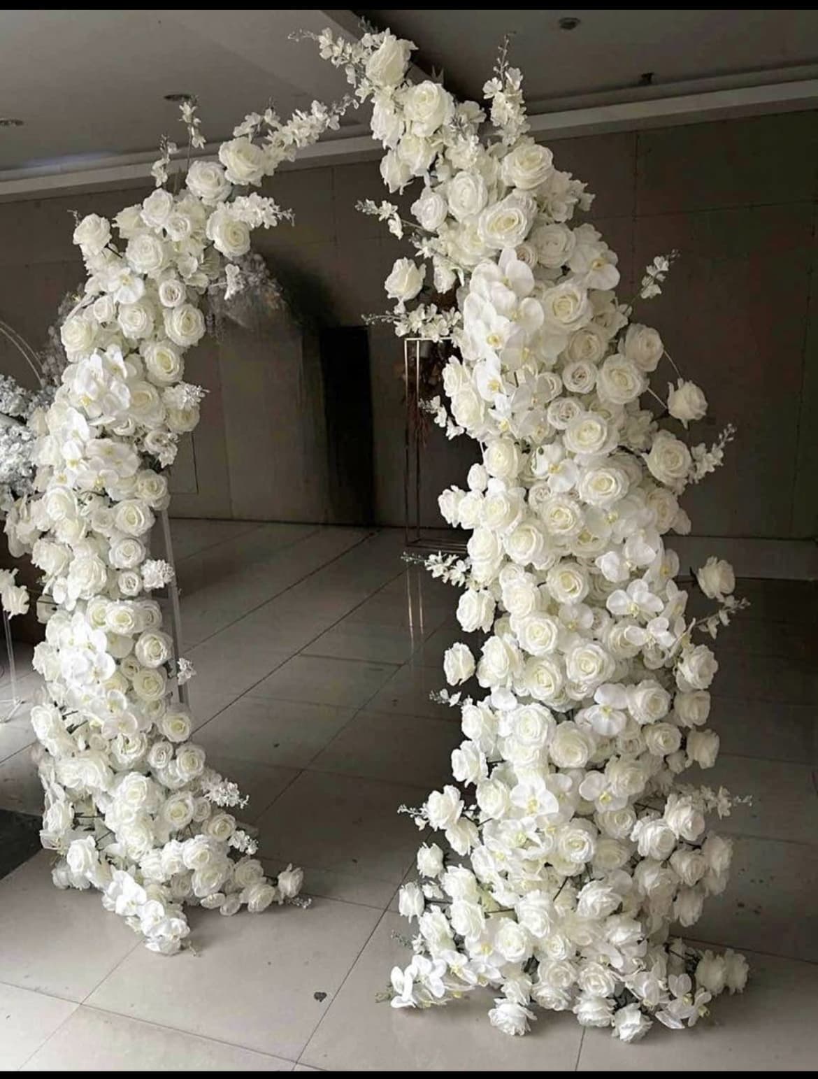 Elegant indoor floral archway composed of thick clusters of white roses and delicate orchids.