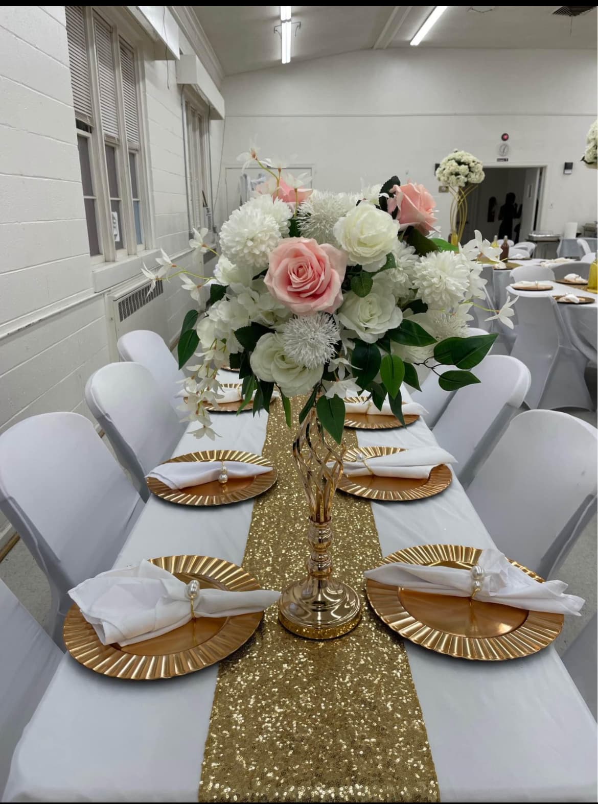Elegant banquet table with gold sequin runner, pink and white floral centerpiece, and gold plates.