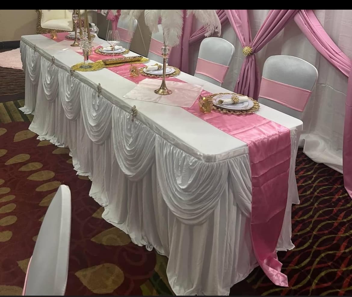 Elegant banquet table with white ruffled linens, pink runners, gold accents, and white feather centerpieces.