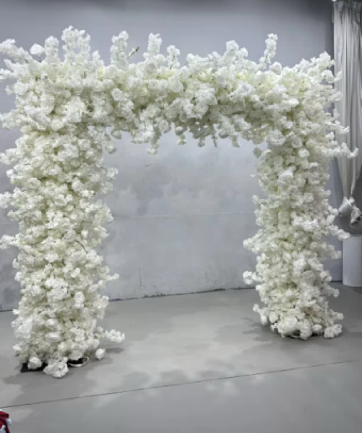 Large rectangular archway densely covered in lush white artificial flowers against a grey background.