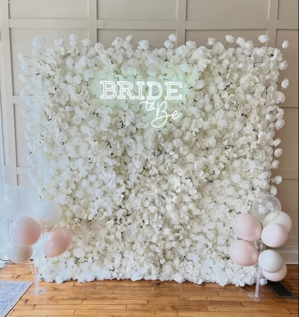 White floral wall with a neon Bride to Be sign and pink and white balloons.