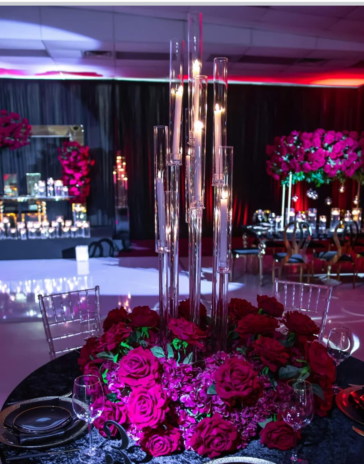 Tall glass candle centerpiece surrounded by vibrant red roses on a formal dinner table.