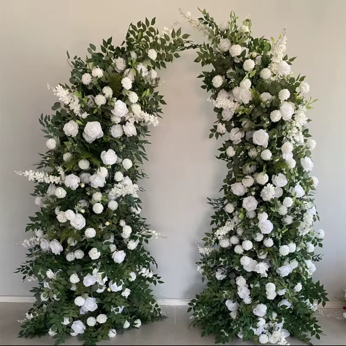 Elegant floral archway featuring lush green foliage and numerous white roses and carnations.