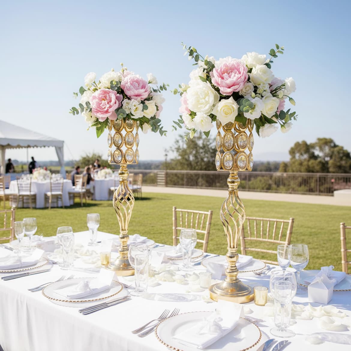 Formal outdoor wedding table featuring tall gold centerpieces with pink and white floral arrangements.