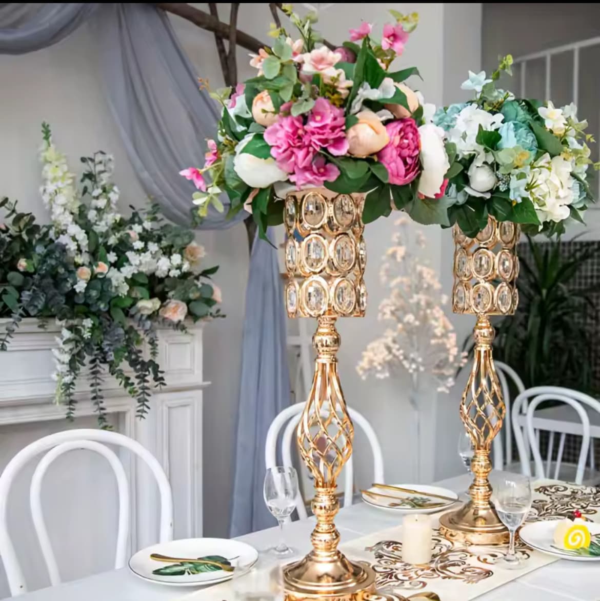 Two tall gold crystal flower stands with colorful floral arrangements on an elegantly set table.
