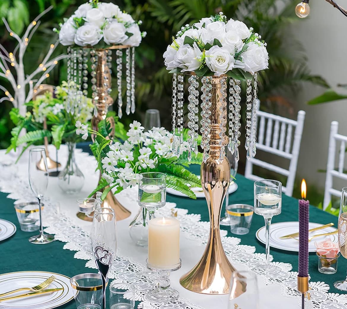 Elegant table setting with gold centerpieces, white roses, hanging crystals, and candles on green cloth.
