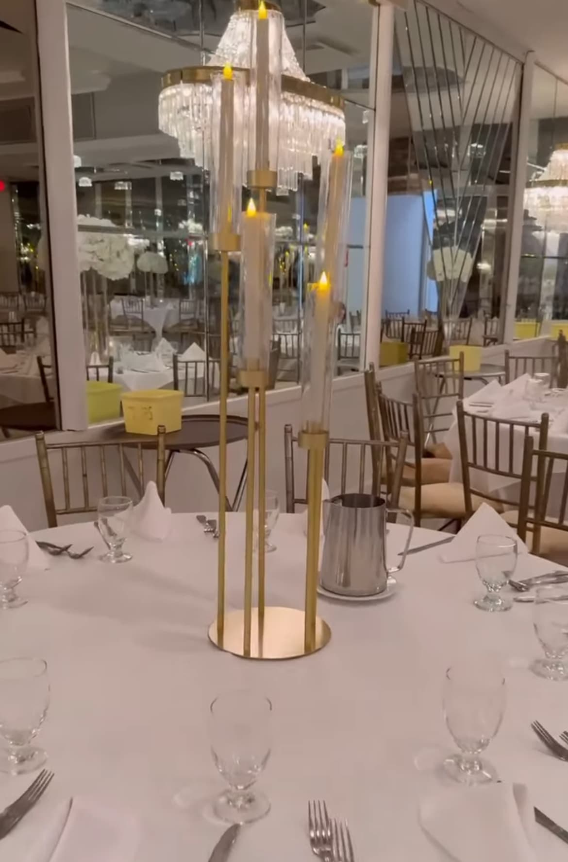 Gold candelabra centerpiece on a white-clothed banquet table in a formal, mirrored event space.