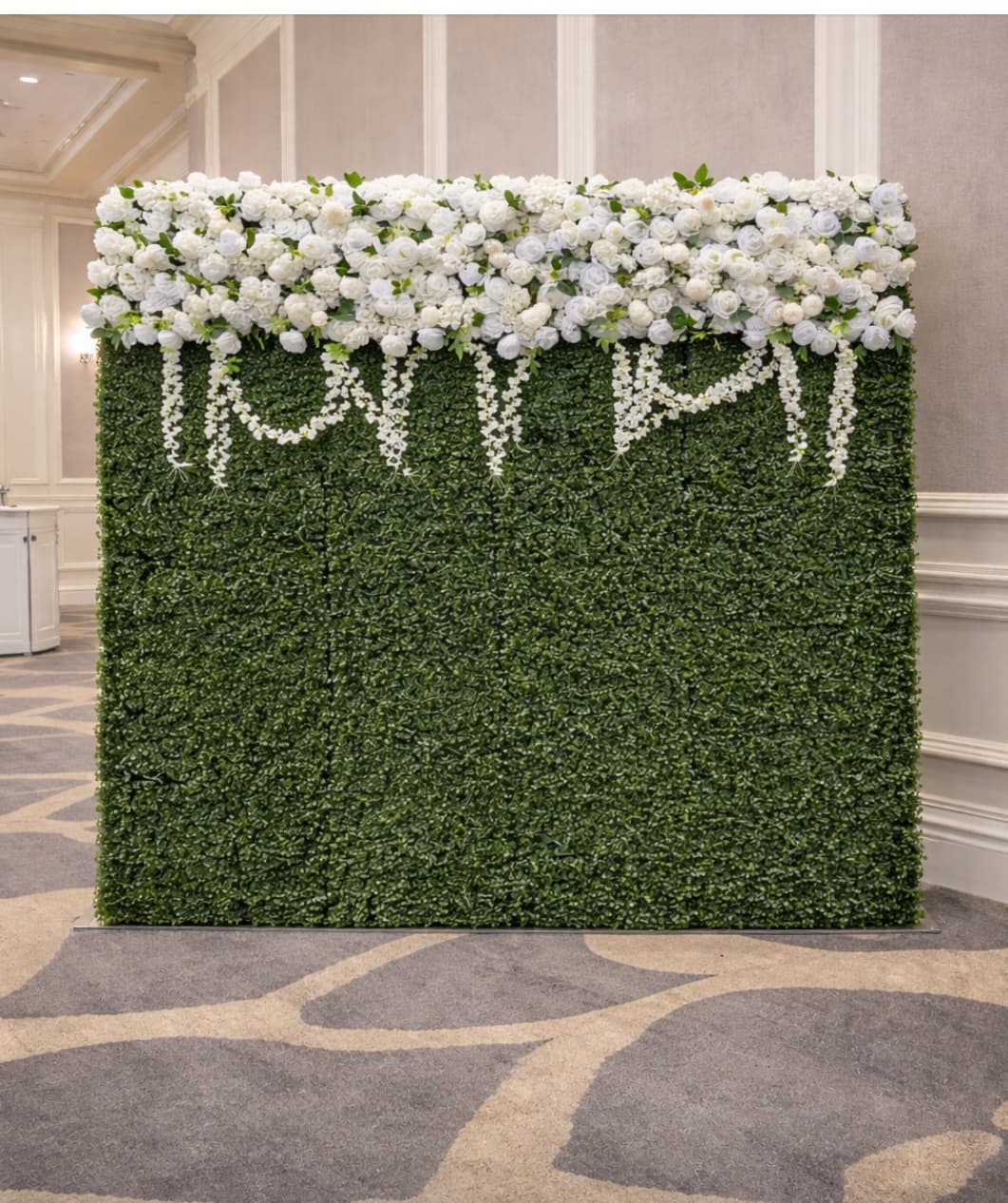 Green boxwood hedge backdrop with a lush white floral top and hanging flower garlands.
