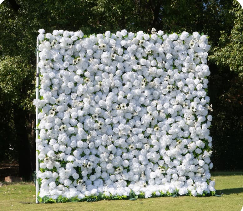 Large square backdrop of white roses and anemones stands on a green lawn outdoors.