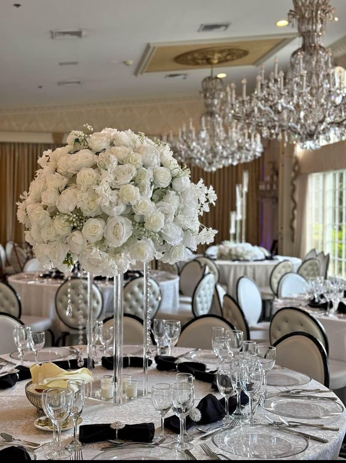 Large white floral centerpiece on a formal dining table in an elegant ballroom with chandeliers.