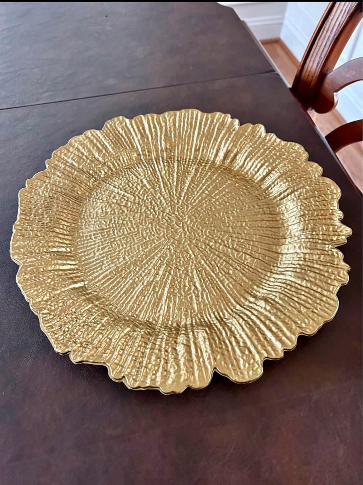 Textured gold charger plate with a sunburst pattern and scalloped edges on a dark table.